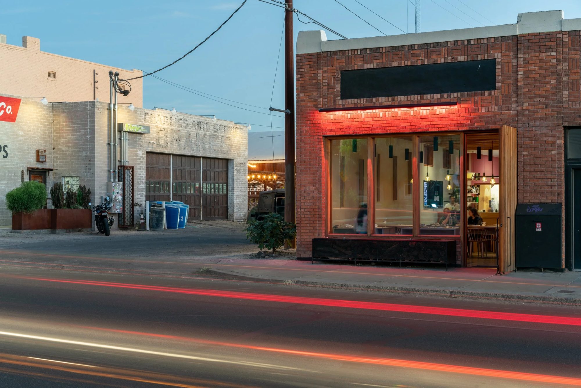 ANELLO’s brick storefront at dusk, a line of red neon glowing above the window and car light trails on 6th Street