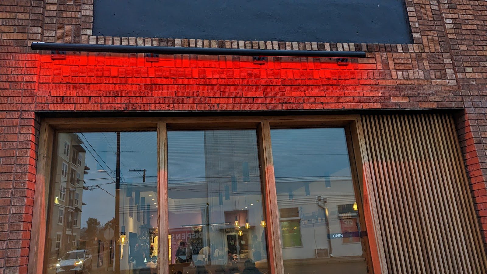 A close view of the storefront window at dusk with the red neon glowing warm against the brick